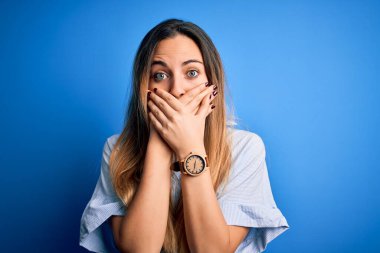 Mavi gömlekli, mavi gözlü, genç, güzel sarışın kadın mavi arka planda, ağzı yanlışlıkla ellerle kapatmış. Gizli konsept.