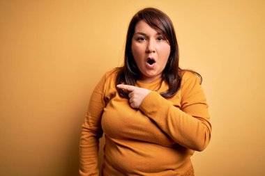 Güzel esmer ve cüsseli bir kadın izole edilmiş sarı arka plan üzerine günlük süveter giyiyor..