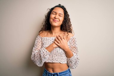 Kıvırcık saçlı, beyaz arka planda dikilen, elleri göğsünde, gözleri kapalı ve yüzünde minnet dolu bir jest olan bir kadın. Sağlık kavramı.
