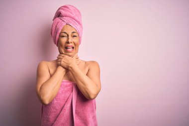 Orta yaşlı bir kadın pembe arka planda güzellik havlusu takıyor bağırıyor ve boğuluyor çünkü acı verici bir boğulma var. Sağlık problemi. Boğulma ve intihar konsepti.