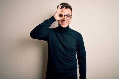 Gözlüklü, gözlüklü, sıradan bir süveter giyen genç, yakışıklı beyaz bir adam. El hareketleriyle gülümsüyor ve mutlu yüzüyle parmaklarından bakıyor..