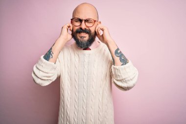 Sakallı, dövmeli, gözlüklü, pembe arka planda süveter giyen, kulaklarını parmaklarıyla kapatan, gürültülü müzik sesi için rahatsız edici ifadeleri olan yakışıklı kel bir adam. Sağır kavramı.