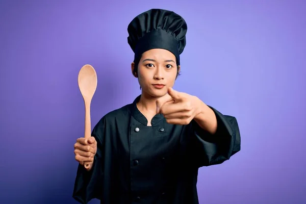 年轻美丽的中国厨师女士身穿炊具制服 头戴木勺 用手指指着相机和你 正面是积极自信的手势 — 图库照片