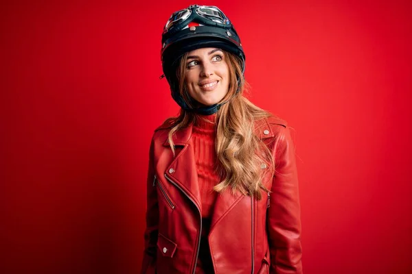 若い美しいブルネットのオートバイの女性が顔に笑顔で横に見える赤い背景の上に元ヘルメットを着て 自然な表情 自信を持って — ストック写真