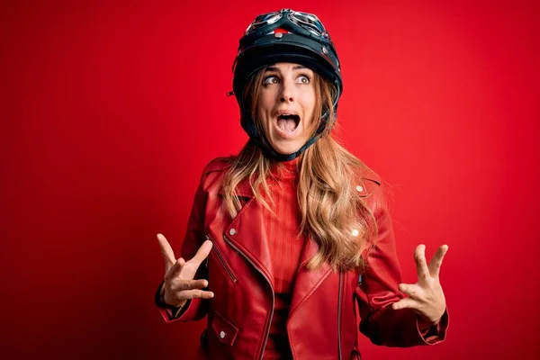 赤の背景に元ヘルメットを身に着けている若い美しいブルネットのオートバイの女性は狂気と怒りの叫びと積極的な表現と腕を上げて叫びました 欲求不満の概念 — ストック写真
