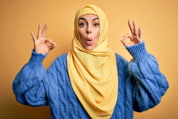 年轻美丽的黑发穆斯林女人 头戴阿拉伯头巾 头戴黄褐色的背景 看上去很惊讶 很震惊 用手指做了个认可的标志 疯狂的表情 — 图库照片