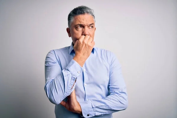 Middle age handsome grey-haired business man wearing elegant shirt over white background looking stressed and nervous with hands on mouth biting nails. Anxiety problem.