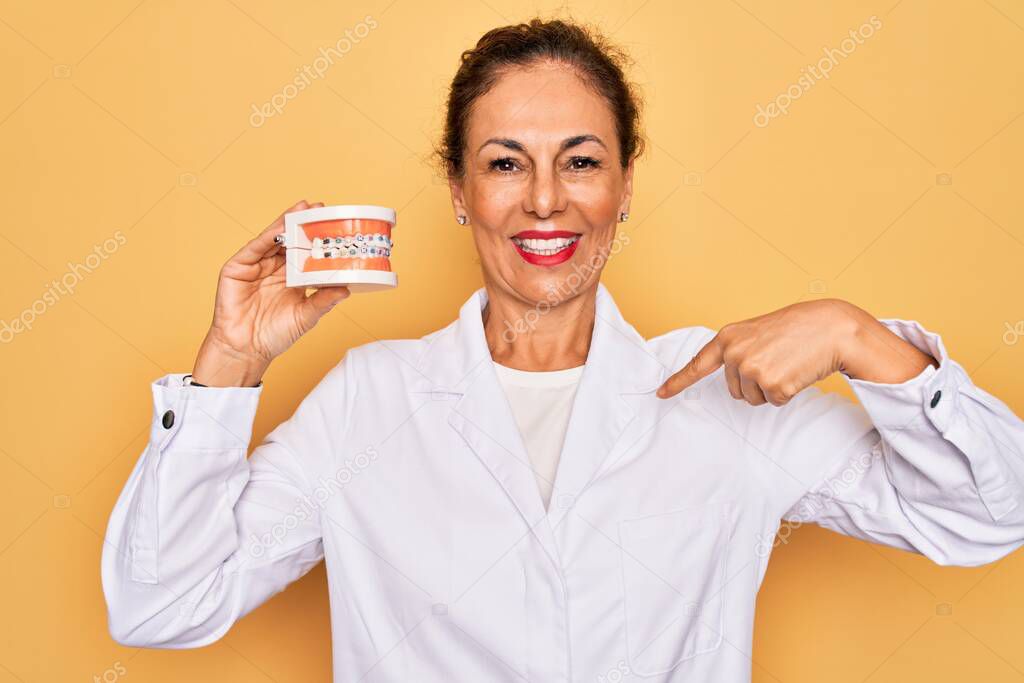 Middle age senior dentist woman holding orthodontics denture with braces aligner with surprise face pointing finger to himself