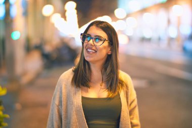 Mutlu ve kendinden emin gülümseyen genç ve güzel bir kadın. Kasaba caddesinde yüzünde gülümsemeyle dikilirken