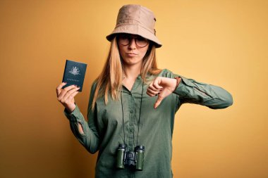 Sarışın, mavi gözlü, elinde Avustralya pasaportu olan, kızgın yüzlü dürbün kullanan, hoşlanmadığını gösteren negatif işaretli, baş parmaklı, reddedilmiş bir turist kadın.