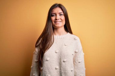 Mavi gözlü genç ve güzel bir kadın sarı arka planda mutlu ve havalı bir gülümsemeyle sıradan bir süveter giyiyor. Şanslı kişi..