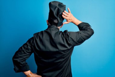 Orta yaşlı, yakışıklı, gri saçlı, aşçı üniformalı ve şapkalı adam. Geriye dönüp, elleri kafasında şüpheyi düşünüyor.