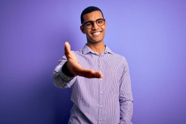 Yakışıklı Afro-Amerikalı adam mor arka planda çizgili gömlek ve gözlük takıyor. Gülümsüyor, avuç içi dolusu yardım ve kabullenme teklif ediyor..