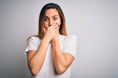 Mavi gözlü, beyaz arka planda sıradan tişörtler giyen genç, güzel sarışın kadın ağzını yanlışlıkla ellerle kapatmış. Gizli konsept.