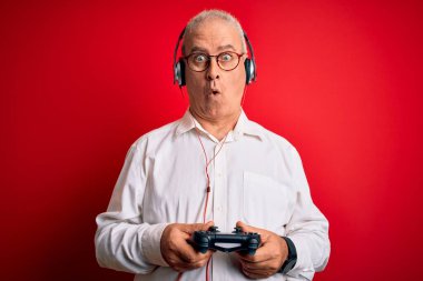 Orta yaşlı yakışıklı beyaz oyuncu joystick ve kulaklık kullanarak oyun oynuyor. Şaşırmış bir yüzle korkmuş ve korku ifadesinden korkmuş.