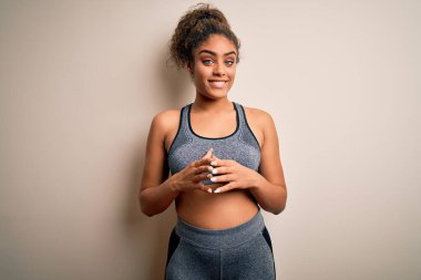 Genç Afro-Amerikan sporcu kadın spor yapıyor beyaz arka planda spor giysisi giyiyor ellerini birleştirip gülümsüyor ve neşeyle gülümsüyor. Başarı ve iyimser