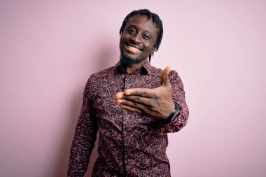 Genç, yakışıklı, Afro-Amerikalı bir adam pembe arka planda dikilmiş gülümsüyor, yardım eli uzatıyor ve kabul ediyor..