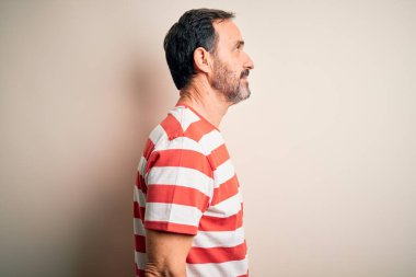 Orta yaşlı, beyaz çizgili tişört giyen, izole edilmiş beyaz arka plan üzerinde duran, rahat bir görünüm takınan, kendine güvenen gülümsemeli, orta yaşlı beyaz bir adam..