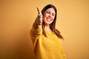 Sarı izole edilmiş arka plan üzerine sıradan bir süveter giyen genç ve güzel bir kadın selamlaşma ve dostça bir selamlama olarak el sıkışma sunuyor. Başarılı bir iş..