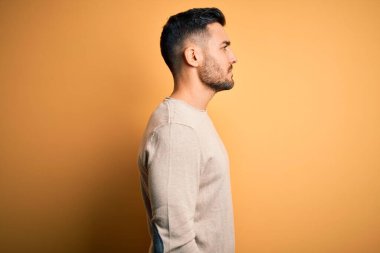 Sarı arka plan üzerinde duran sıradan bir süveter giyen genç yakışıklı bir adam yan tarafa bakıyor, rahat bir görünüm sergiliyor kendine güvenen bir gülümsemeyle doğal bir yüz ifadesi sergiliyor.