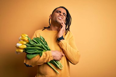 Genç Afro-Amerikan Afro-Amerikan romantik adam elinde sarı lale buketiyle diş ağrısı ya da diş ağrısı yüzünden ağızlarına acı dolu bir ifadeyle dokunuyor. Dişçi konsepti.