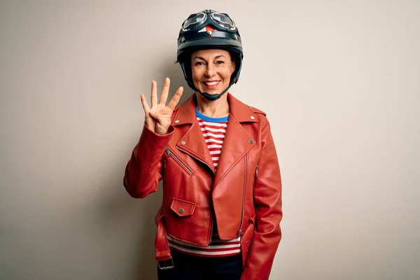 中年オートバイの女性身に着けていますオートバイヘルメットとジャケット上の白い背景表示と指差しますとともに指番号4ながら笑顔自信と幸せ — ストック写真