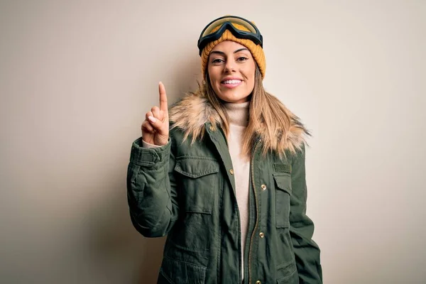 若いブルネットのスキーヤーの女性は 成功したアイデアで指を指す白い背景の上に雪の服とスキーゴーグルを身に着けています 興奮し 第一番 — ストック写真