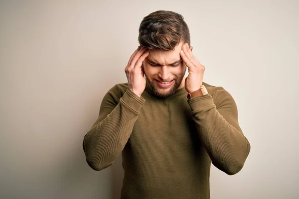 stock image Young blond man with beard and blue eyes wearing green sweater over white background with hand on head for pain in head because stress. Suffering migraine.