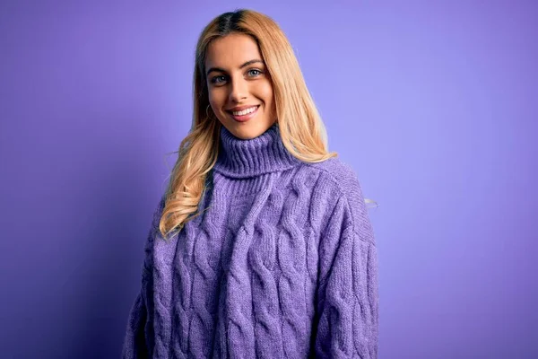 若い美しいブロンドの女性は 顔に幸せとクールな笑顔で紫色の背景にカジュアルなタートルネックセーターを着ています 運のいい人 — ストック写真