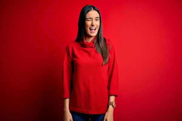 Young beautiful brunette woman wearing casual sweater over isolated red background winking looking at the camera with sexy expression, cheerful and happy face. — Stock Image Young Beautiful Brunette Woman Wearing Casual Sweater Isolated Red Background Stock Image