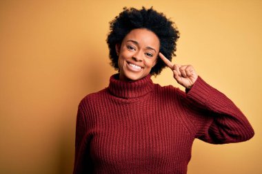 Kıvırcık saçlı, balıkçı yaka kazaklı, güzel Afro-Amerikan bir kadın. Tek parmağıyla başını gösteren gülümsüyor. Harika bir fikir ya da düşünce, iyi bir hafıza.