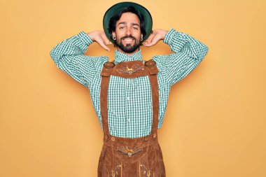 Almanya Festivali için geleneksel Alman Ekim Festivali geleneği giyinen yakışıklı genç adam rahatlıyor ve esniyor, kolları ve elleri başının arkasında mutlu bir şekilde gülümsüyor.