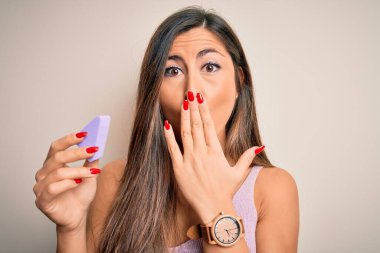 Güzel bir kadın pembe arka plan üzerinde yüz makyajı ile güzellik süngeri kullanıyor. Ağzı kapalı, elleri utançla dolu, hata yüzünden şok olmuş, korku ifadesi, sessizlikten korkmak, gizli bir konsept.