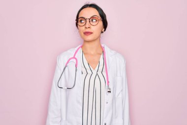 Pembe arka planda mavi gözlü, steteskop takmış, gülümseyen ve kafasını çeviren güzel doktor kadın..