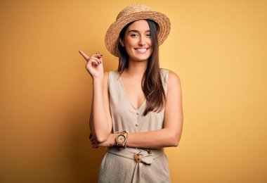 Genç, güzel, esmer kadın tatilde. Sıradan elbiseler ve şapkalar giyiyor. Yüzünde kocaman bir gülümseme var..