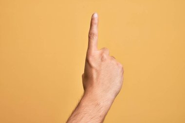 İzole edilmiş sarı arka planda parmaklarını gösteren beyaz bir gencin eli işaret parmağı kullanarak bir numarayı sayıyor, fikir ve anlayış gösteriyor.