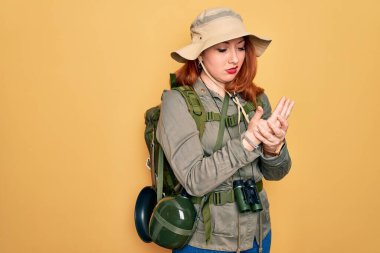 Sırt çantalı, şapkalı, sarı arka planda gezen kızıl saçlı genç bir kadın. Ellerinde ve parmaklarında ağrı var. Eklem iltihabı.