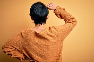 Sarı arka planda dikilen, gündelik süveter ve diyabet giyen Asyalı genç ve güzel bir kız. Geriye doğru, elleri kafasında şüpheyi düşünüyor.