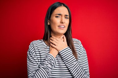 Genç, güzel esmer kadın kırmızı arka planda sıradan çizgili tişört giyip boğularak can çekişiyor çünkü boğularak ölüyor. Sağlık problemi. Boğulma ve intihar konsepti.