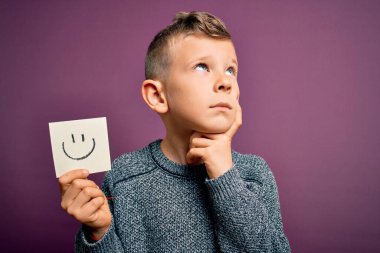 Küçük beyaz bir çocuk kağıtta gülen surat ile mutlu bir mesaj veriyor. Yüzü ciddi ciddi soruyla dolu, kafası karışmış bir fikir.