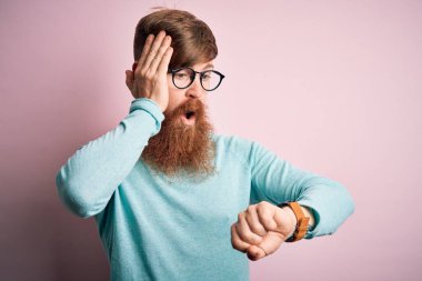 Sakallı, pembe soyutlanmış arka planda gözlük takan yakışıklı kızıl saçlı, endişeli ve geç kalmaktan korkan bir adam.