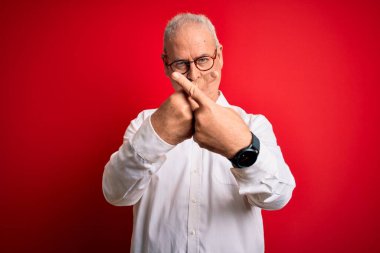 Orta yaşlı, yakışıklı, beyaz gömlekli ve kırmızı arka planda gözlüklü bir adam. Reddedilme ifadesi olumsuz işaret veriyor.