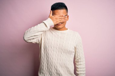 Beyaz süveter giyen, pembe arka planda gözlük takan, gülümseyen ve gülen genç, yakışıklı Latin bir adam. Kör kavram.