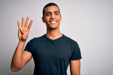 Genç ve yakışıklı Afro-Amerikalı adam beyaz arka planda dikilen ve parmaklarını dört numarayı gösterirken kendinden emin ve mutlu bir şekilde gülümsüyor..