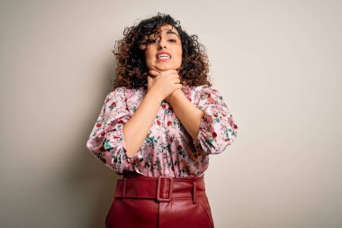 Genç ve güzel kıvırcık Arap kadın çiçekli tişört giyip izole edilmiş beyaz arka planda dikiliyor ve boğularak ölüyor çünkü acı verici bir boğulma var. Sağlık problemi. Boğulma ve intihar konsepti.