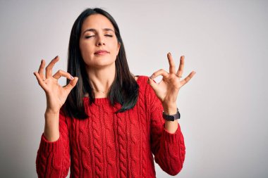 Mavi gözlü genç esmer kadın izole edilmiş beyaz arka planda günlük süveter giyiyor rahatlamış ve parmaklarıyla meditasyon hareketi yaparken gözleri kapalı gülümsüyor. Yoga konsepti.