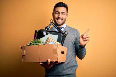 Ofis kasası tutan genç bir iş adamı sarı arka plandan kovuluyor. Çok mutlu bir şekilde elini ve parmağını yana uzatıyor.