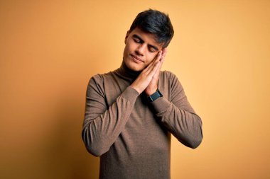 Sarı arka planda günlük balıkçı yaka kazak giyen genç yakışıklı adam uyur, yorgun düşler kurar ve elleri ile birlikte poz verir, kapalı gözlerle gülümserdi..