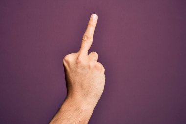 Hand of caucasian young man showing fingers over isolated purple background showing provocative and rude gesture doing fuck you symbol with middle finger