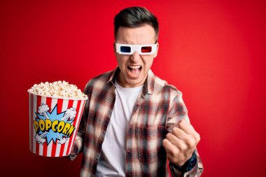 Üç boyutlu film gözlüğü takan yakışıklı beyaz bir adam kızgın ve kızgın patlamış mısır yiyor öfkeyle bağırırken yumruğunu sallıyor ve öfkeleniyor. Öfke ve agresif kavram.